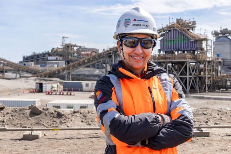 Trabajadora minera con casco y ropa de seguridad frente a una planta de procesamiento.